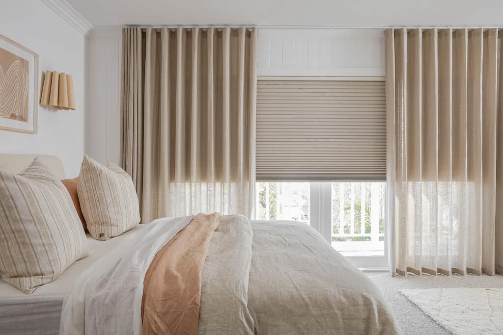 Organic earth-toned aesthetic bedroom featuring large window covered with Luxaflex Shutters with Curtains. Available at Complete Blinds showroom.