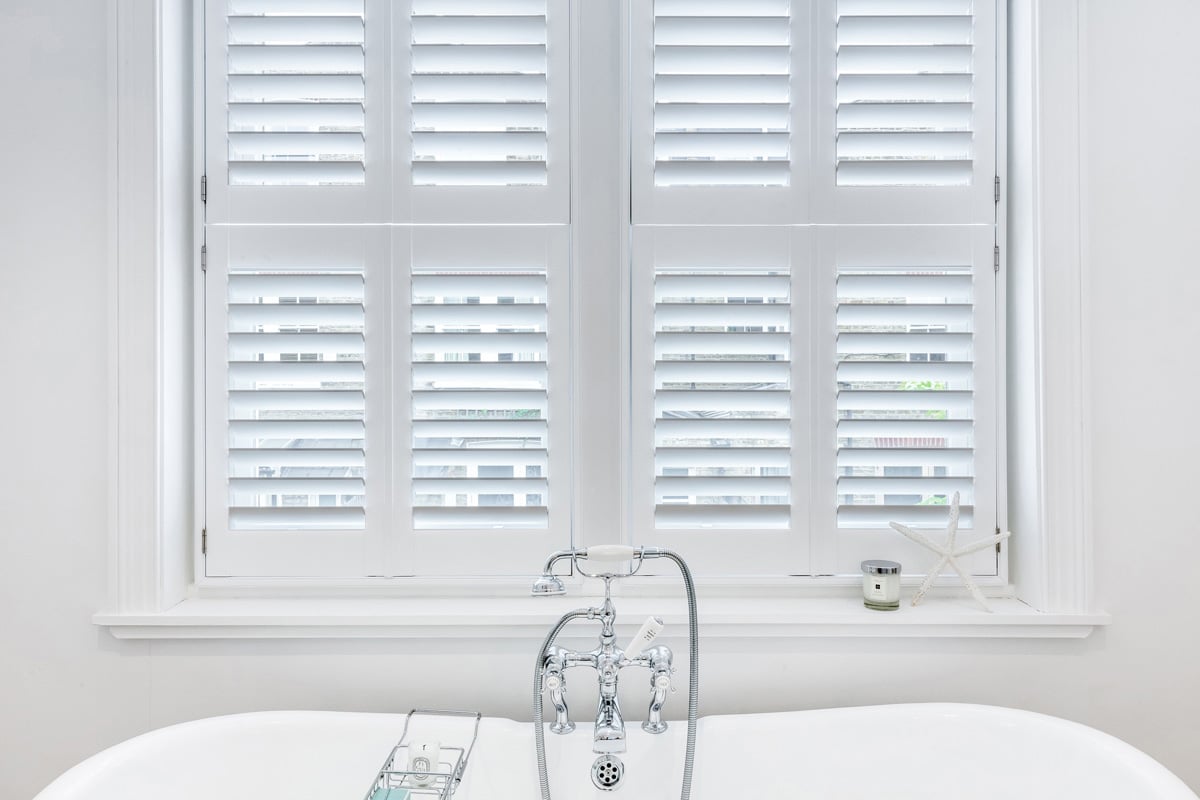 White Plantation Shutters installed in a white classical-themed bathroom.