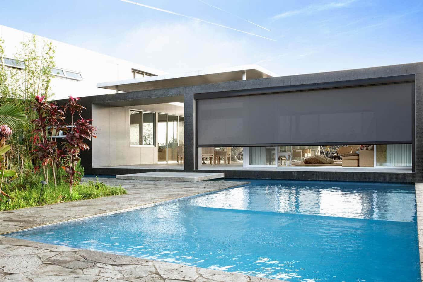 Modern luxurious home with swimming pool, featuring dark grey Evo Magnatrack Awnings by Luxaflex installed at the patio.