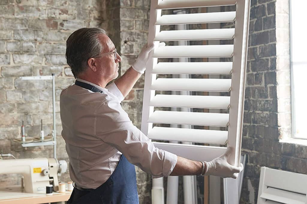 A sophisticated Luxaflex craftsman holding a Luxaflex window blind, customising to fit the window frame perfectly. Made in Australia.