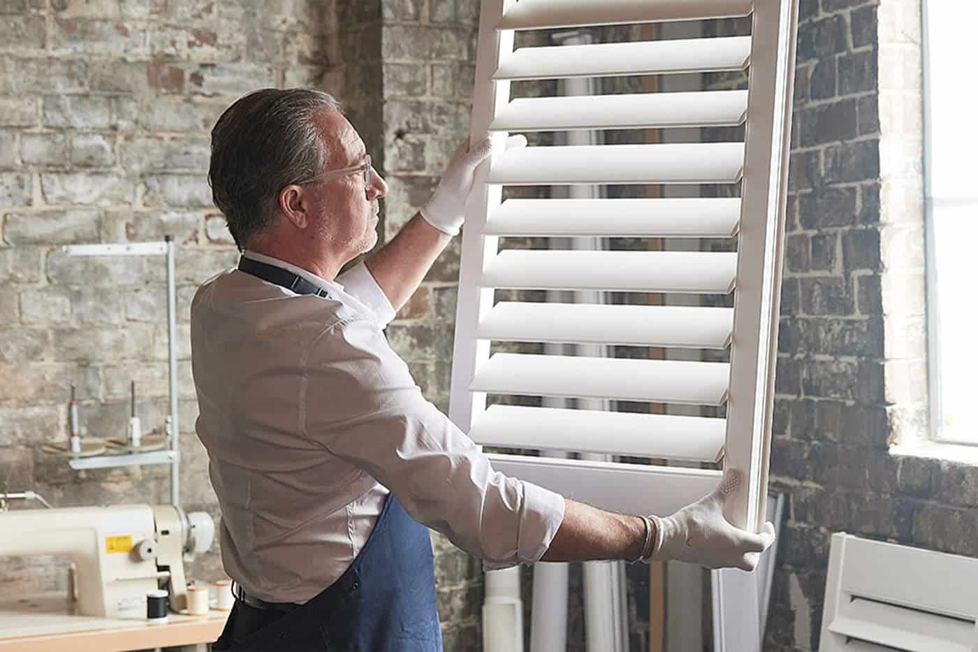 A sophisticated Luxaflex craftsman holding a Luxaflex window blind, customising to fit the window frame perfectly. Made in Australia.
