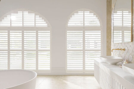 Classic Transitional Style White Bathroom With Large Radius Windows Covered By Luxaflex Polysatin Shutters, Offering Light And Privacy Control In The Bathroom. Suitable For Wet Areas. For Sale In Our Sydney Showroom.