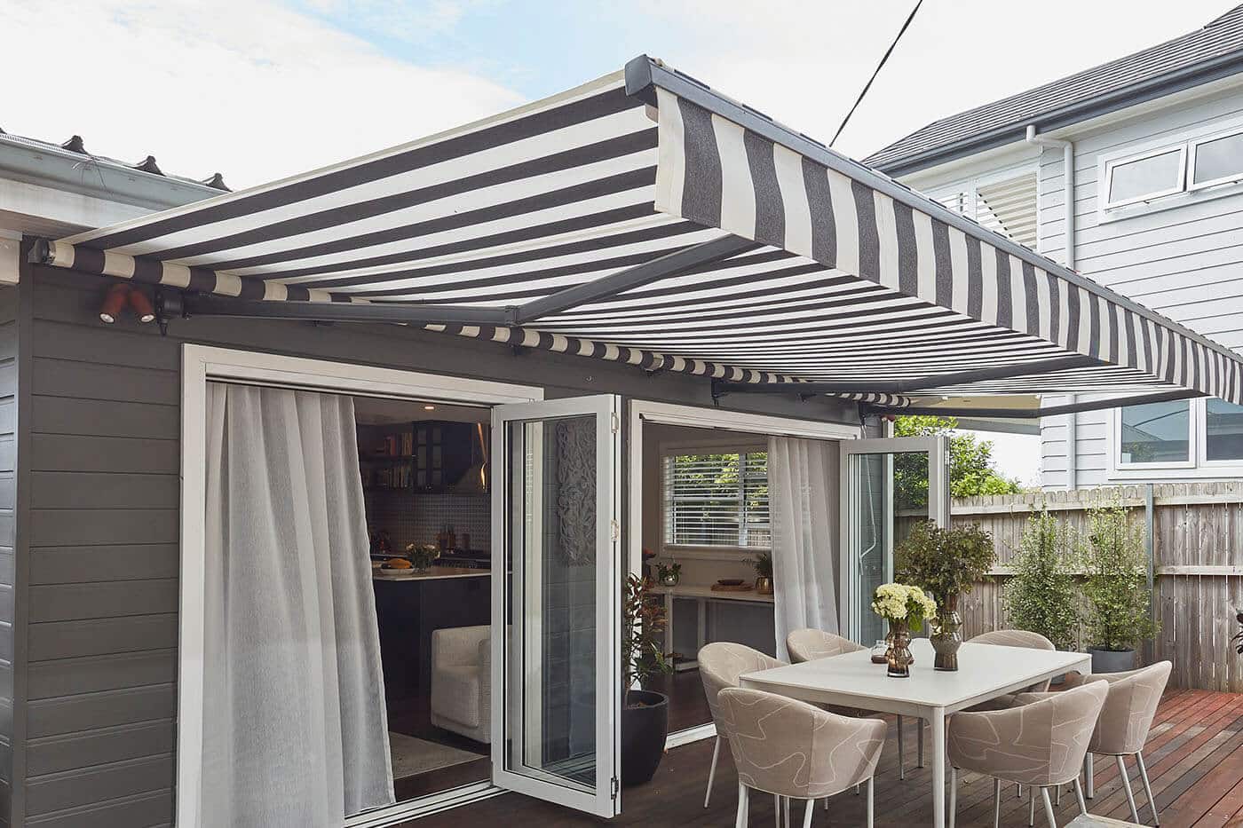 Patio of mid-century home style with dinning table, covered by a Motorised Folding Arm Awning by Luxaflex. It can be retracted too. Made in Australia.