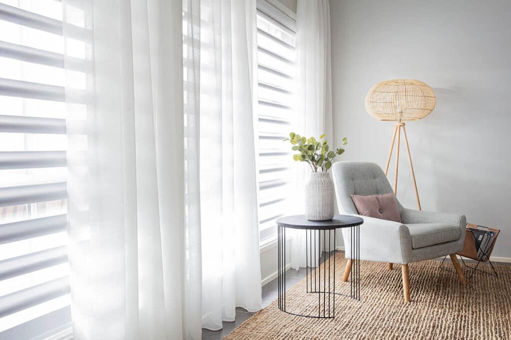 Contemporary living space with comfortable chair and floor rug, featuring Luxaflex sheer curtains partially covering window panes, diffusing natural light and giving the room an atmospheric look. How to Measure Windows for Curtains.