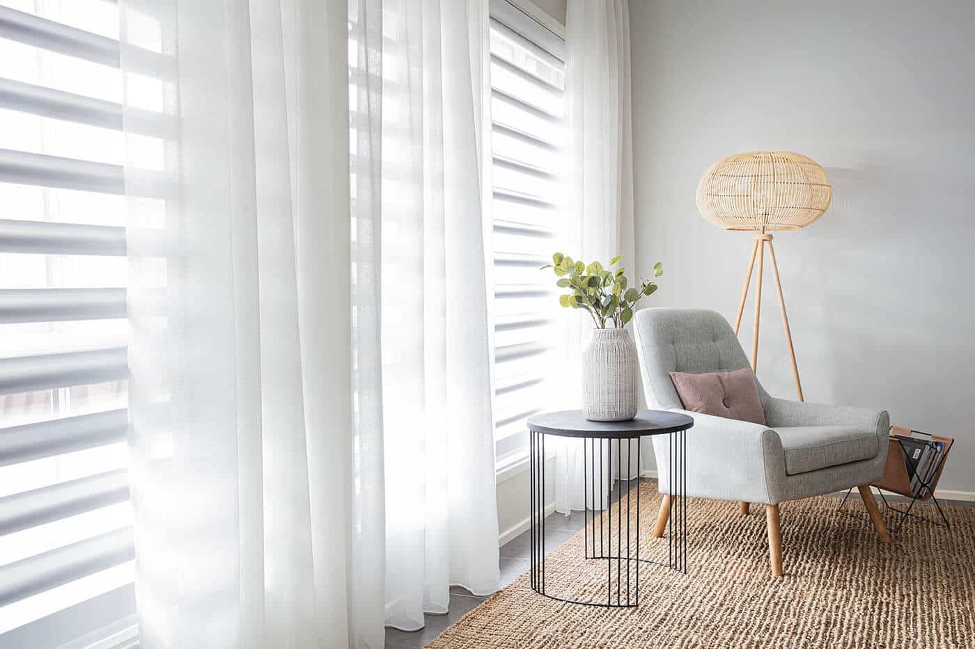 Contemporary living space with comfortable chair and floor rug, featuring Luxaflex sheer curtains partially covering window panes, diffusing natural light and giving the room an atmospheric look.