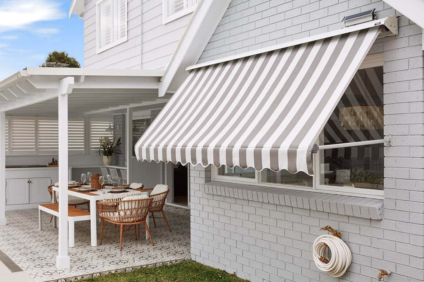 Outside view of a home patio and garden with mid-century design style, featuring Luxaflex System 2000 Awning covering a big window pane, providing shade and blocking out sunlight. On display in our Sydney showroom.