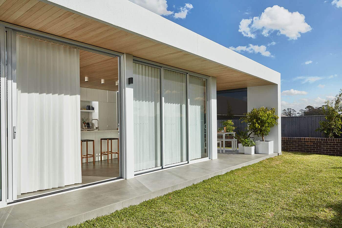 Modern house with large windows and greenery outside. Windows are partly covered by Luxaflex LumiShade, controlling the amount of natural light entering the home. Made in Australia.