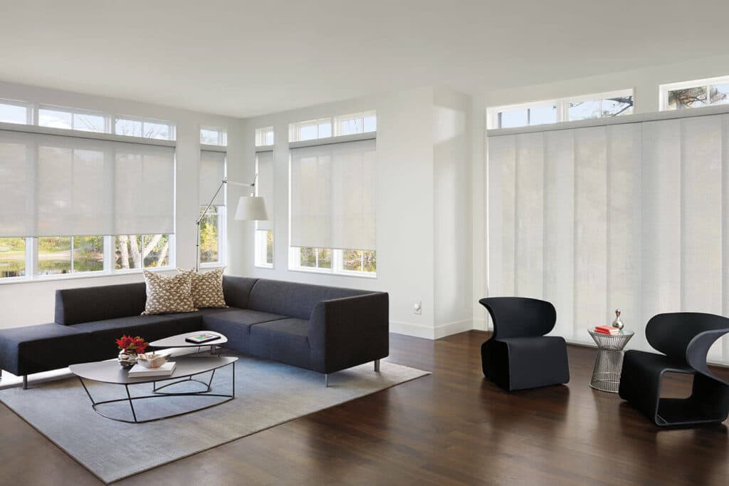 Wide contemporary living space with modern furniture designs, featuring Luxaflex Panel Glide Blinds cover several large window panes, diffusing natural light into the room.