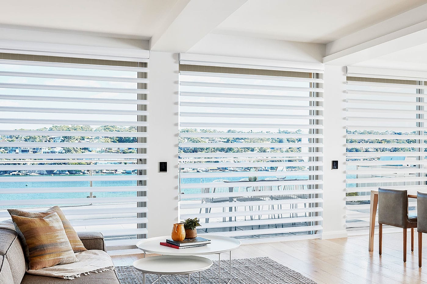 Pirouette shadings delivering the appearance of floating fabric vanes in a brightly lit living room, with sea view and yacht in the background.