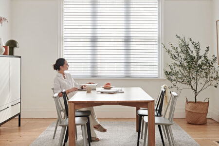 A Lady Enjoying Her Magazine In A Nicely-lit Room Filled With Natural Sunlight, Simple And Elegant Interior Design With Wood And Plants, Featuring Luxaflex Silhouette Shades.