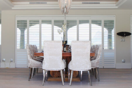 Modern Traditional White Themed Dining Area With Wooden Table, Featuring Normandy Shutters By Norman. Available At Complete Blinds Sydney.