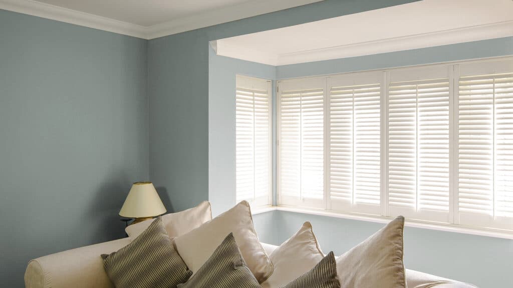 Bay windows in bedroom installed with white window shutters by Complete Blinds Sydney for privacy control. 